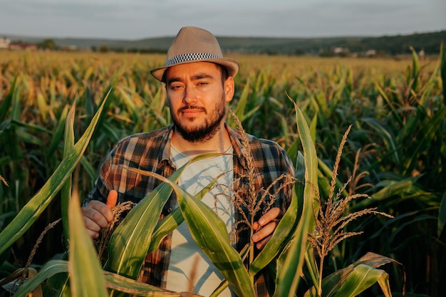 Вид спереди, смотрящий в камеру, серьезный усталый молодой фермер стоит на кукурузном поле