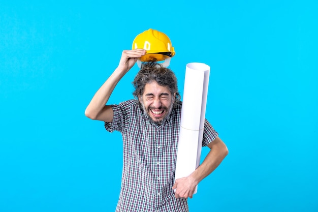 Front view male builder in helmet holding plan on the blue background job architecture engineer building color constructor skyscraper