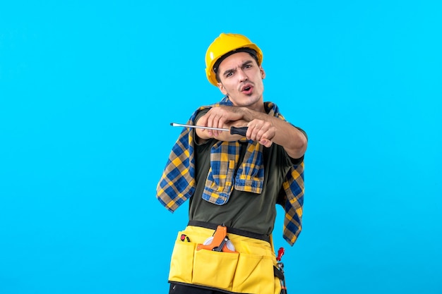 front view male builder in helmet holding screwdriver on the blue background flat architecture house job building worker constructor