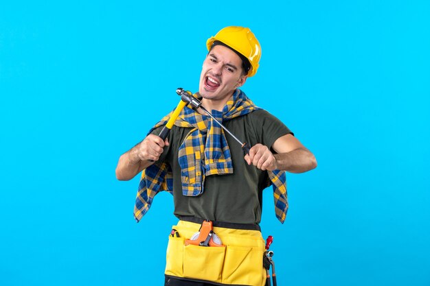 front view male builder in helmet holding screwdriver and hammer on a blue background flat house job building worker constructor