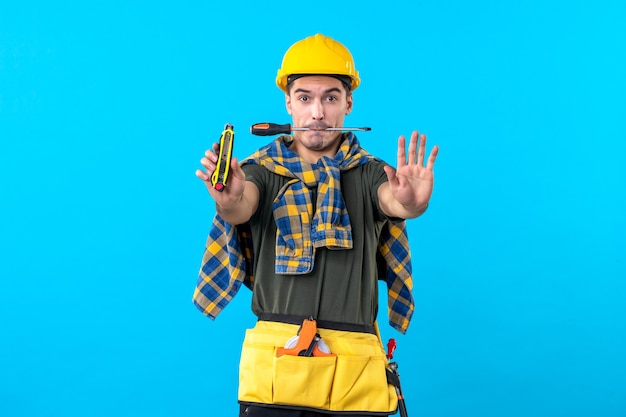 front view male builder in helmet holding screwdriver with his mouth on blue background flat architecture house job building constructor