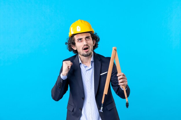 front view male builder in helmet holding wooden device on blue background job business constructor architecture building work