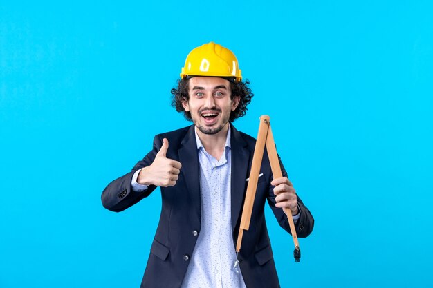 front view male builder in helmet holding wooden device on blue background job business constructor architecture buildings work design