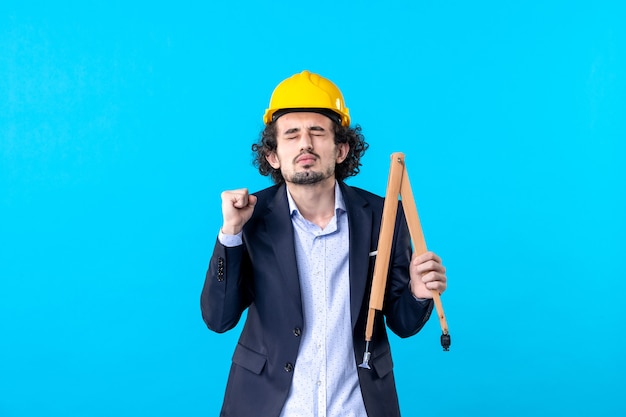 front view male builder in helmet holding wooden device on blue background job business constructor building work design