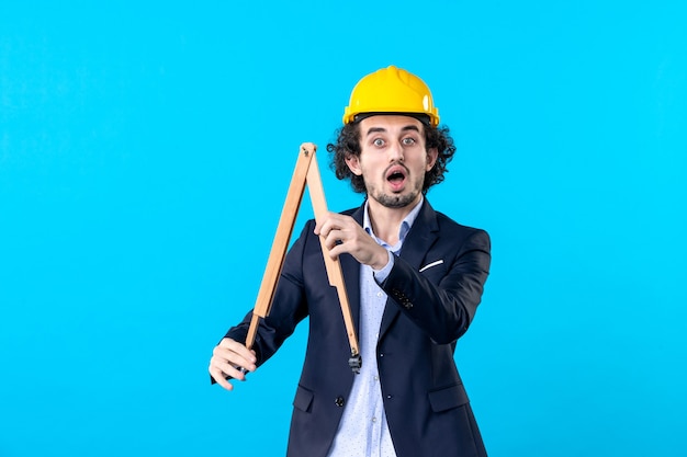 front view male builder in helmet holding wooden geometric figure on blue background work building job business design constructor