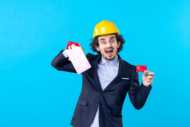 front view male builder holding bank card and sale writing on a blue background job business architecture constructor building work money