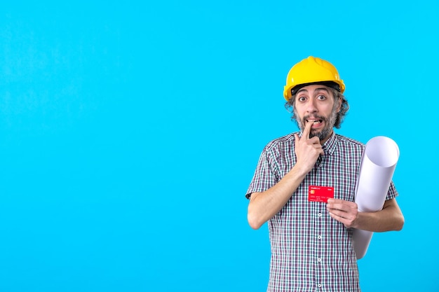 Front view male builder holding plan and bank card on blue background money design constructor building job helmet work colors architecture