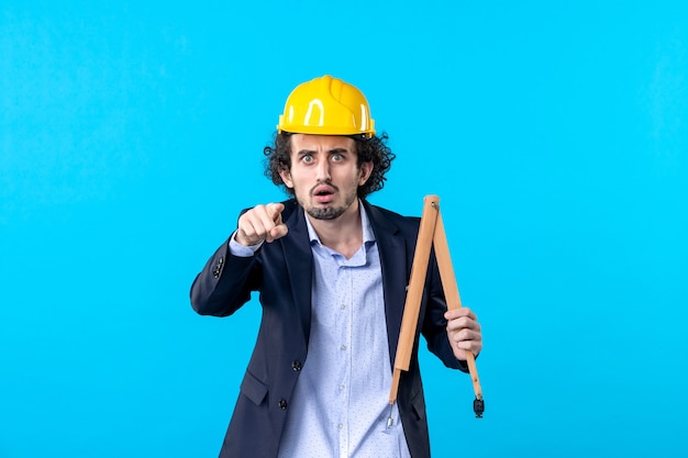 front view male builder holding wooden device on a blue background job business design constructor architecture building work