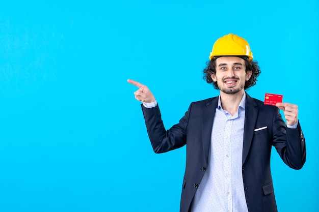 front view male builder in suit holding red bank card on blue background business architecture constructor job money work builder engineer