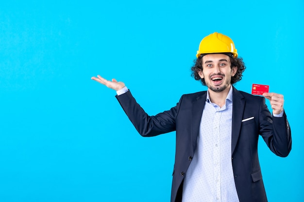 front view male builder in suit holding red bank card on blue background business architecture constructor job work builder engineer