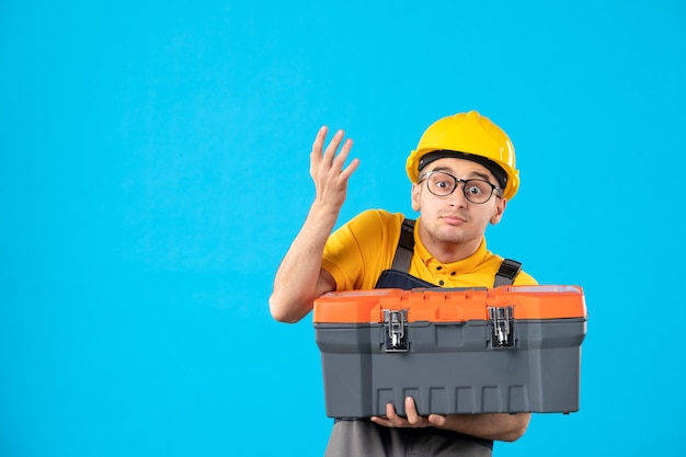 Front view of male builder in uniform with tool box in his hands on blue wall