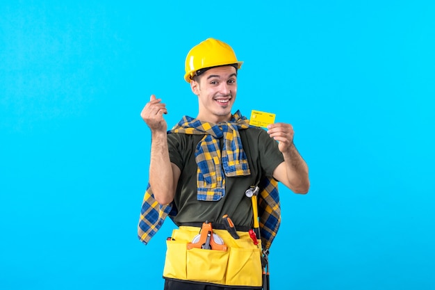 Vista frontale costruttore maschio in casco giallo tenendo la carta bancaria su sfondo blu denaro colore architettura edifici lavoratore costruttore flat