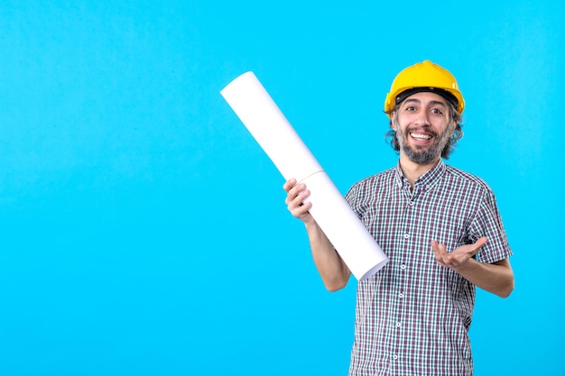 Front view male builder in yellow helmet with plan on blue background building constructor property worker engineer job