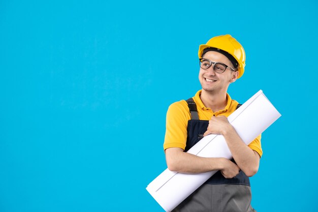 Front view of male builder in yellow uniform and helmet with plan on blue wall
