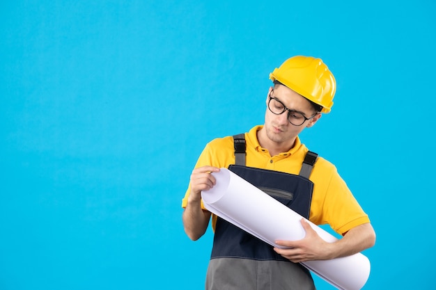 Front view male builder in yellow uniform with paper plan on blue 