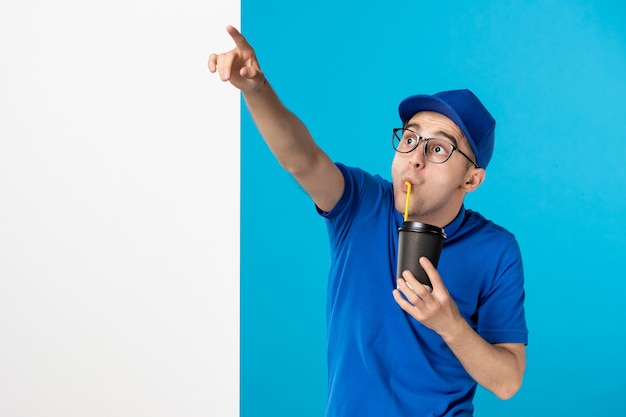 Front view of male courier in uniform with delivery coffee drinking on a blue 