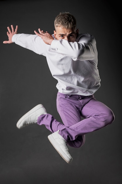 Foto vista frontale del ballerino maschio in jeans viola e scarpe da ginnastica in posa a mezz'aria