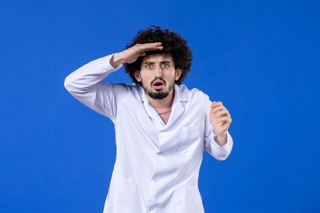 Front view of male doctor in medical suit on blue background vaccine virus covid- pandemic coronavirus medicine drug hospital