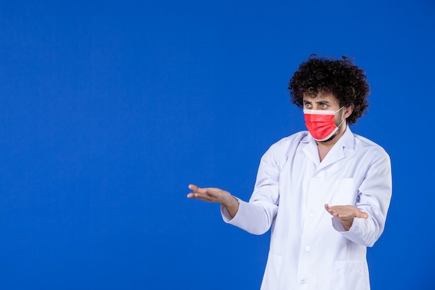 Vista frontale del medico maschio in tuta medica e maschera su sfondo blu vaccino salute covid- coronavirus virus pandemia medicina ospedale farmacologico