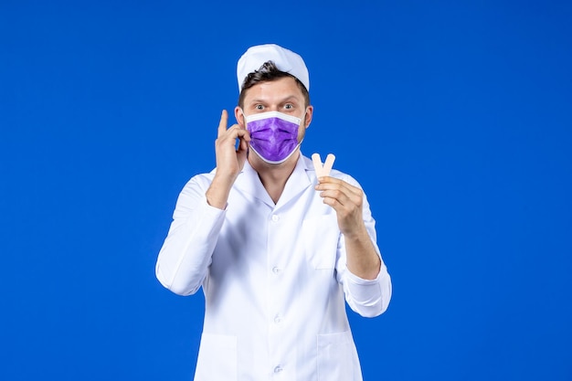 Front view of male doctor in medical suit and mask holding little medical patches on blue 