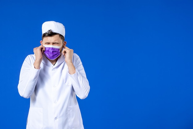 Front view of male doctor in medical suit and purple mask on blue 
