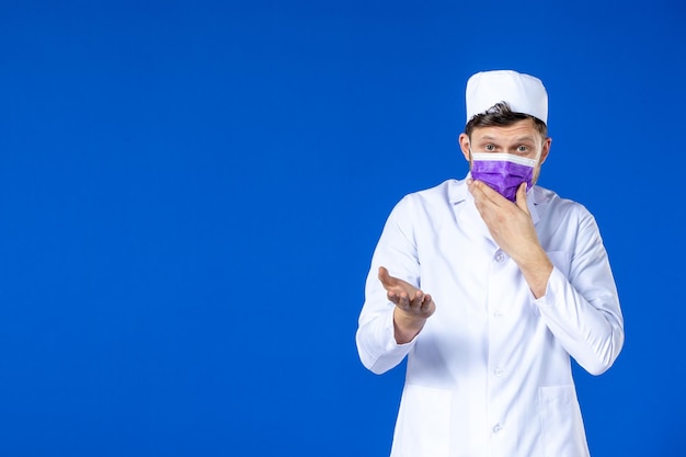 Vista frontale del medico maschio in tuta medica e maschera viola sull'azzurro