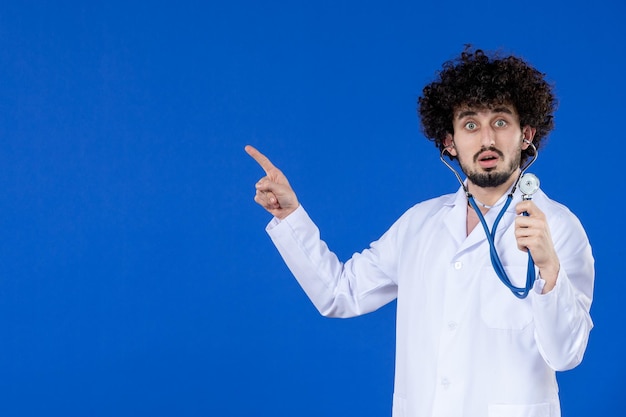 Vista frontale del medico maschio in tuta medica con stetoscopio su sfondo blu salute pandemia covid- coronavirus farmaci vaccino virus ospedale