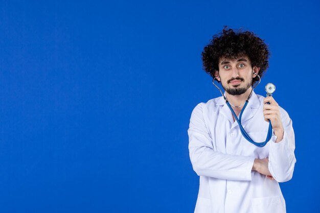 Front view of male doctor in medical suit with stethoscope on blue surface