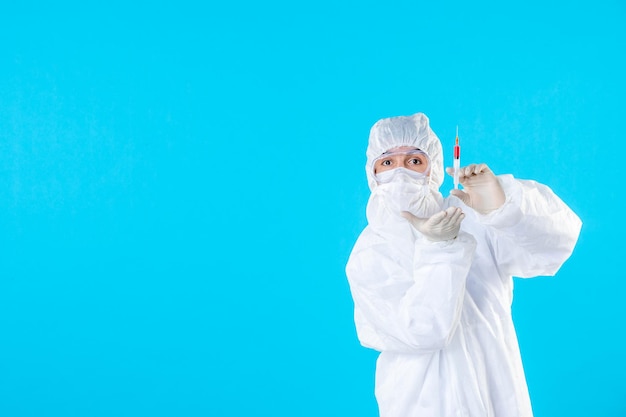 Front view male doctor in protective suit holding injection on blue