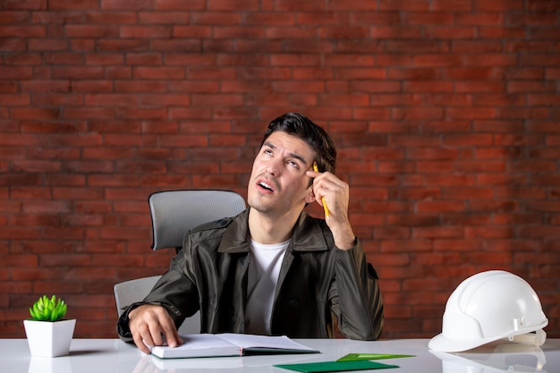 Front view male engineer sitting behind his working and thinking place job business contractor agenda builder property document plan corporate