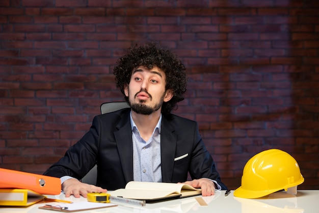 Vista frontale dell'ingegnere maschio seduto dietro il posto di lavoro in tuta appaltatore piano occupazione lavoro progetto business lavoro aziendale