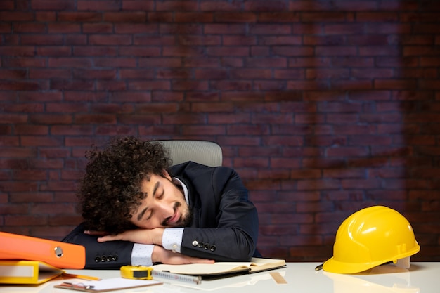 Vista frontale dell'ingegnere maschio seduto dietro il posto di lavoro in tuta e appaltatore addormentato lavoro piano di occupazione aziendale progetto di lavoro aziendale