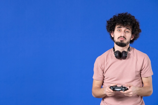 Front view male gamer playing video game with gamepad on blue\
background sofa virtual joy player teen young soccer adult\
winning