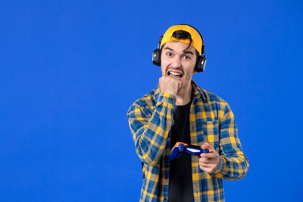 Photo front view of male gamer with gamepad and headphones playing video game on blue wall