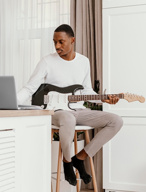 Foto vista frontale del musicista maschio che suona la chitarra elettrica e utilizzando il computer portatile