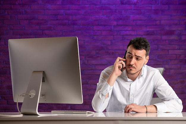 Front view male office worker sitting behind his working place talking