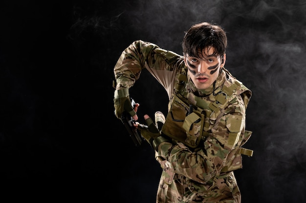 Front view of male soldier in camouflage with gun on black wall