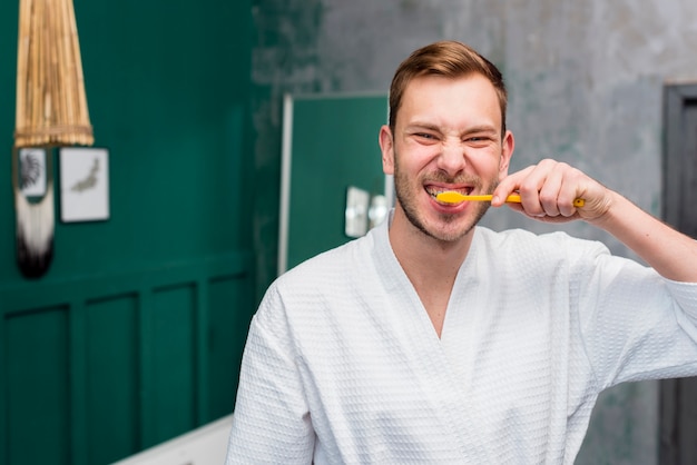 Front view of man in bathrobe brushing his teeth