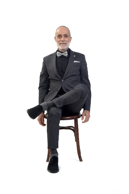 Front view of a man sitting on chair with suit and bow tie and cross legged on white background