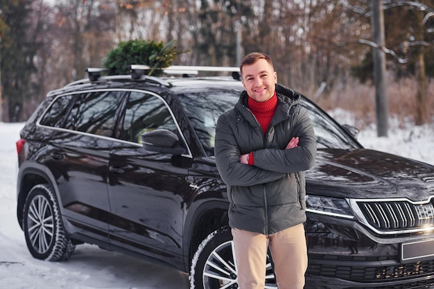 Front view man with little green fir is outdoors near his car
conception of holidays