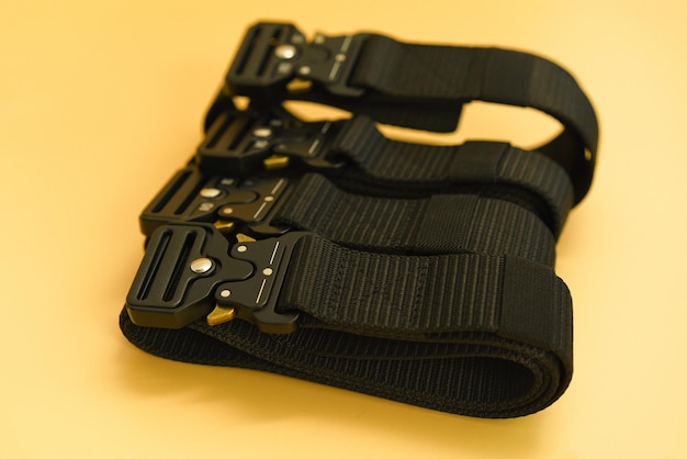 A front view of many black canvas belts with a black fast open\
metal male buckle and a black belt loop lays in the yellow\
background belt military buckle clothing equipment canvas\
protection