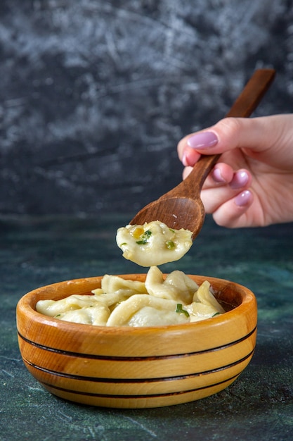Front view meat dumplings with female putting wooden spoon into it on dark surface