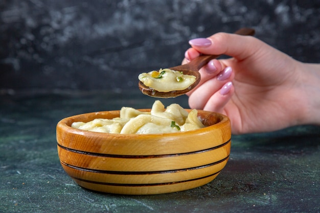 Photo front view meat dumplings with female putting wooden spoon into it on dark surface