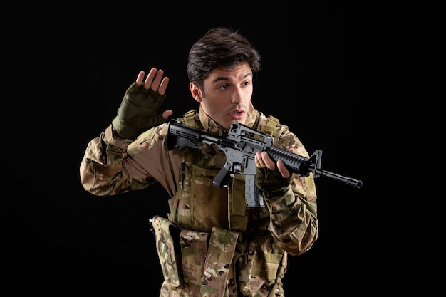 Vista frontale del militare in uniforme che punta il suo fucile in studio sul muro nero