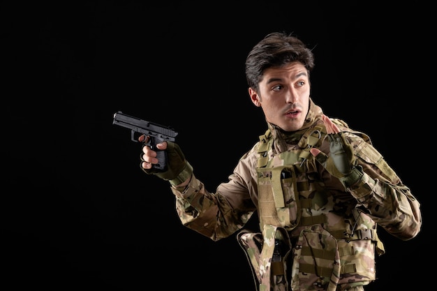 Front view military serviceman in uniform holding gun on black wall