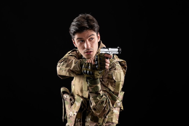 Front view military serviceman in uniform holding gun on black wall