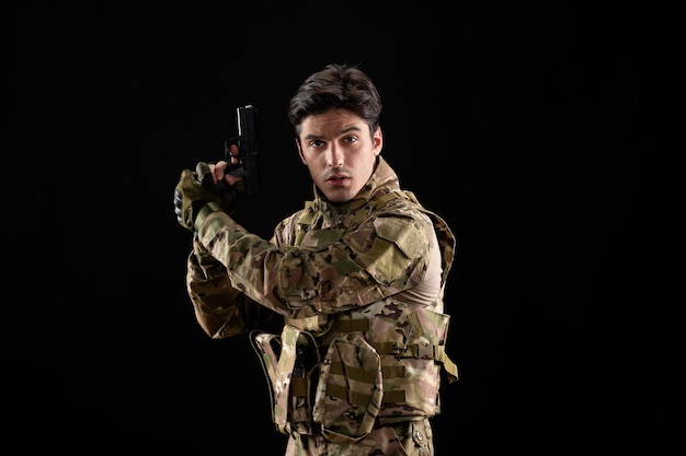 Front view of military serviceman in uniform with gun on black wall