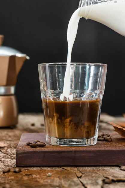 Foto vista frontale latte che viene versato in vetro con caffè