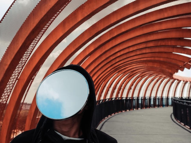 Photo front view of a mirror faced young man standing on a pedestrian bridge