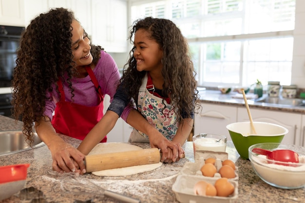 写真 クリスマスに若い娘と一緒にキッチンでクッキーを作り、お互いを見つめる混血女性の正面図